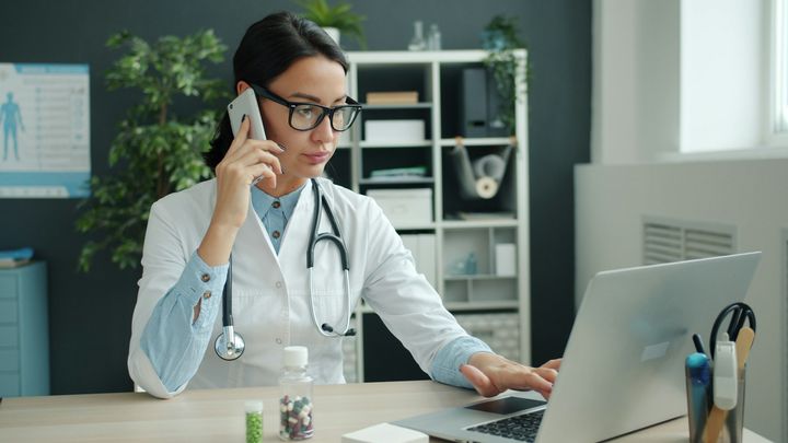 Doctor taking a phone call while answering messages on the computer